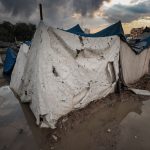 Abrigo de lona danificado em uma área alagada de um campo de refugiados em Gaza, sob céu carregado.