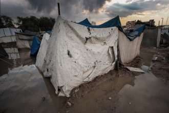 Abrigo de lona danificado em uma área alagada de um campo de refugiados em Gaza, sob céu carregado.