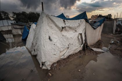 Abrigo de lona danificado em uma área alagada de um campo de refugiados em Gaza, sob céu carregado.