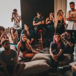 Grupo diverso de pessoas reunido em um espaço amplo, ouvindo atentamente uma mulher durante uma discussão.