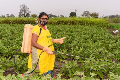 Agricultora usando equipamento de proteção enquanto aplica pesticida em uma plantação.