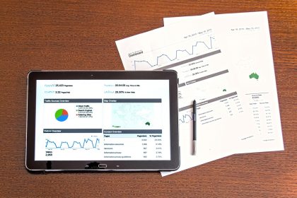 Computador, documentos e gráficos sobre uma mesa de trabalho, representando análise de informações e elaboração de relatório.